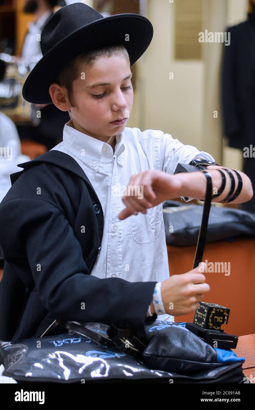 Un ragazzo ebreo ortodosso mette il suo teillin prima dei servizi di preghiera mattutini presso una sinagoga a Crown Heights, Brooklyn, New Yourk. Foto Stock