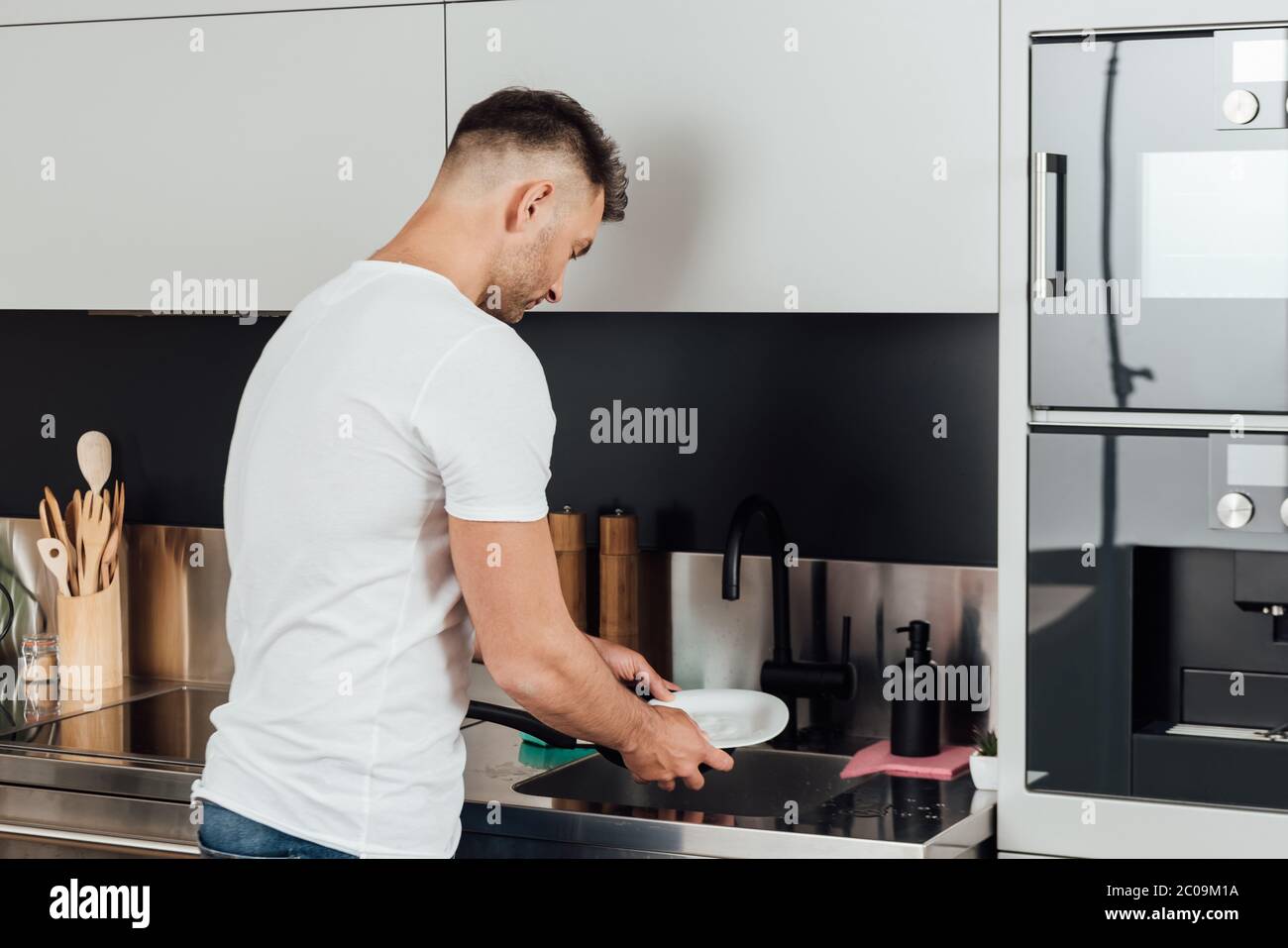 bell'uomo in piedi e lavando piatto bagnato in cucina Foto Stock