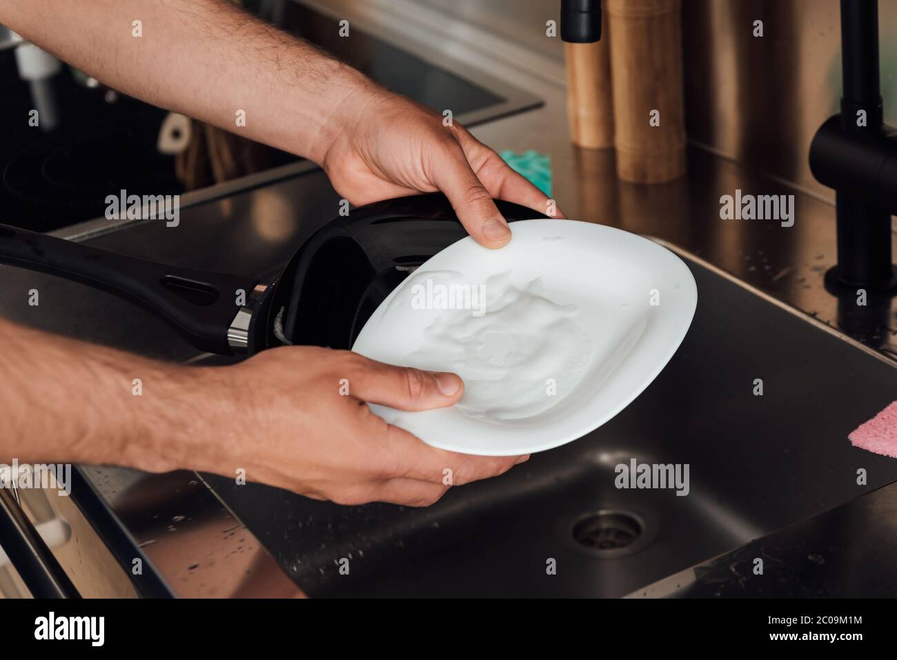 vista tagliata di un uomo che tiene piatto bagnato e padella vicino lavello in cucina Foto Stock