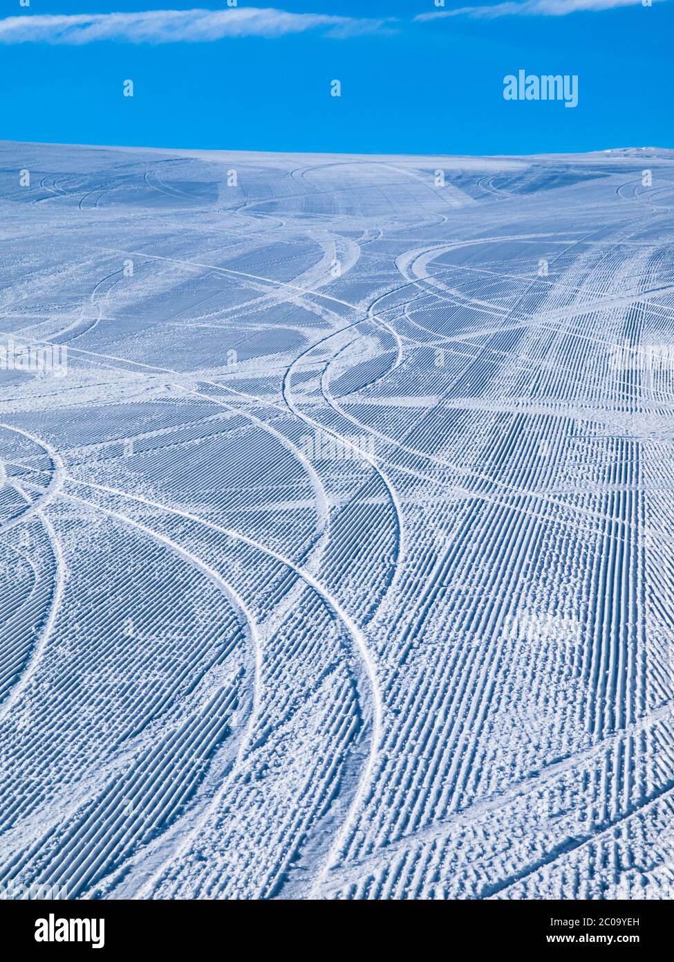 Pista da sci vuota al mattino curata da numerosi tracciati da sciatori e cielo blu Foto Stock