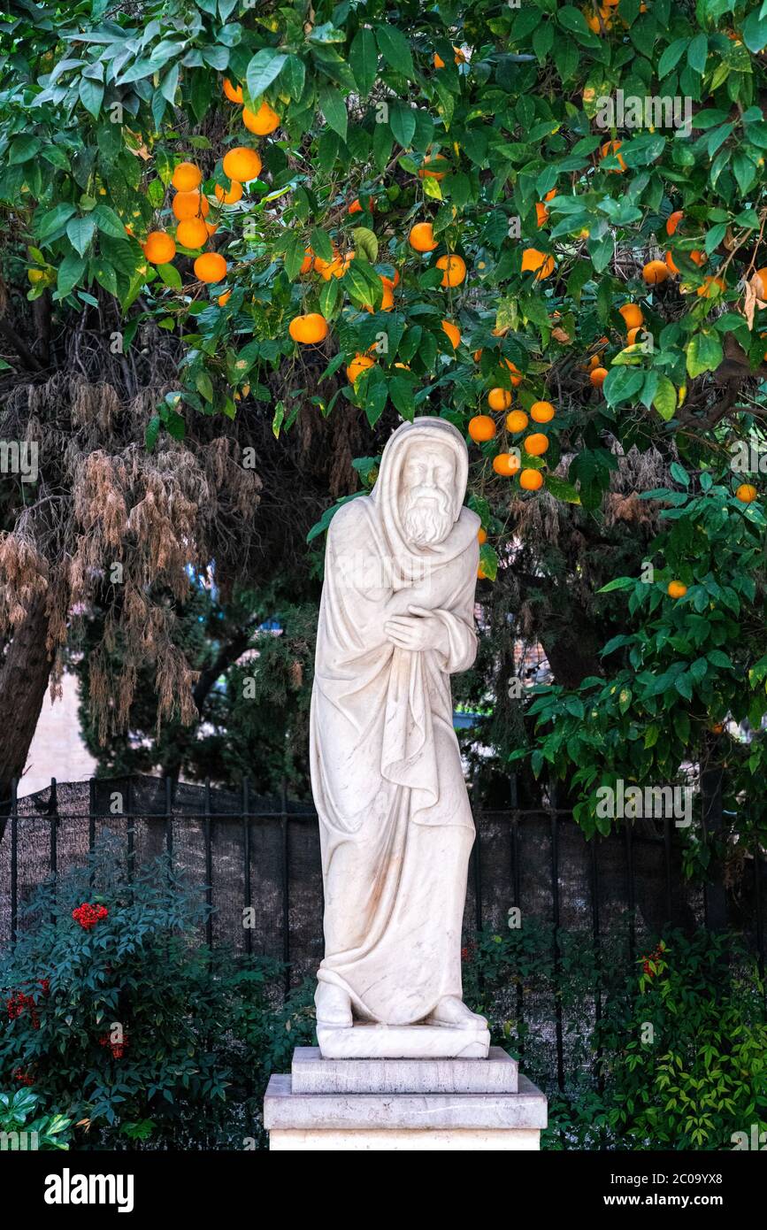 30 dicembre 2019 - Malaga, Spagna. Una statua di un monaco sotto l'albero arancione fuori la fortezza di Alcazaba. Foto Stock