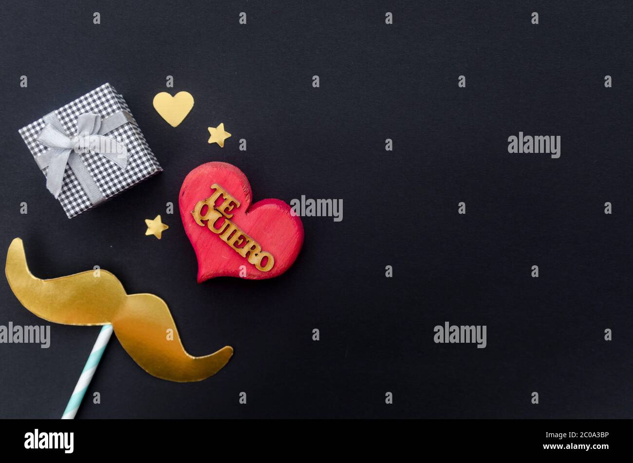 Concetto del giorno del Padre - dono, baffi, cuore e stelle su sfondo nero con la parola in spagnolo per 'ti amo'. Disposizione piatta, vista dall'alto, spazio per la copia. Foto Stock