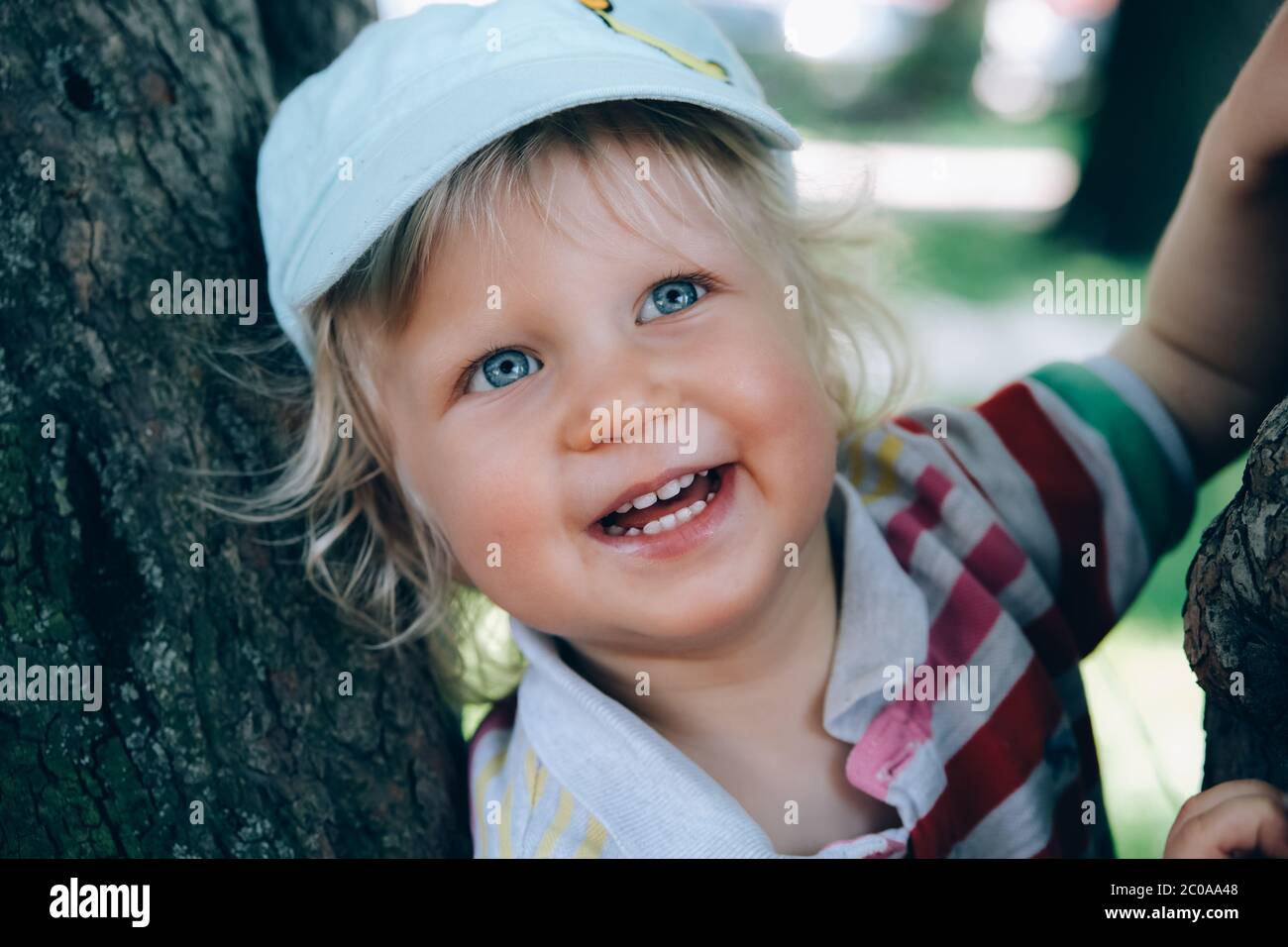 Ritratto di un simpatico ragazzo felice con capelli biondi e occhi blu, che cita un cappello, sorride e gioca nel parco. Torna al concetto normale. Foto Stock