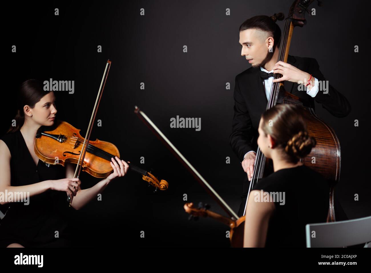 trio di musicisti professionisti che suonano su strumenti musicali su palcoscenico scuro Foto Stock