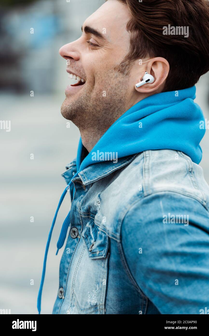 Vista laterale dell'uomo felice negli auricolari che ridono all'aperto Foto Stock