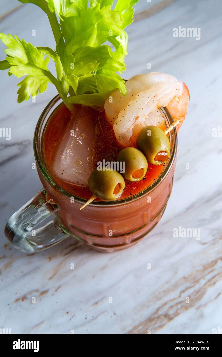 Cocktail di vodka Mary sanguinosa in una birra stein con guarnitura di gamberi su tavolo da cucina in marmo Foto Stock