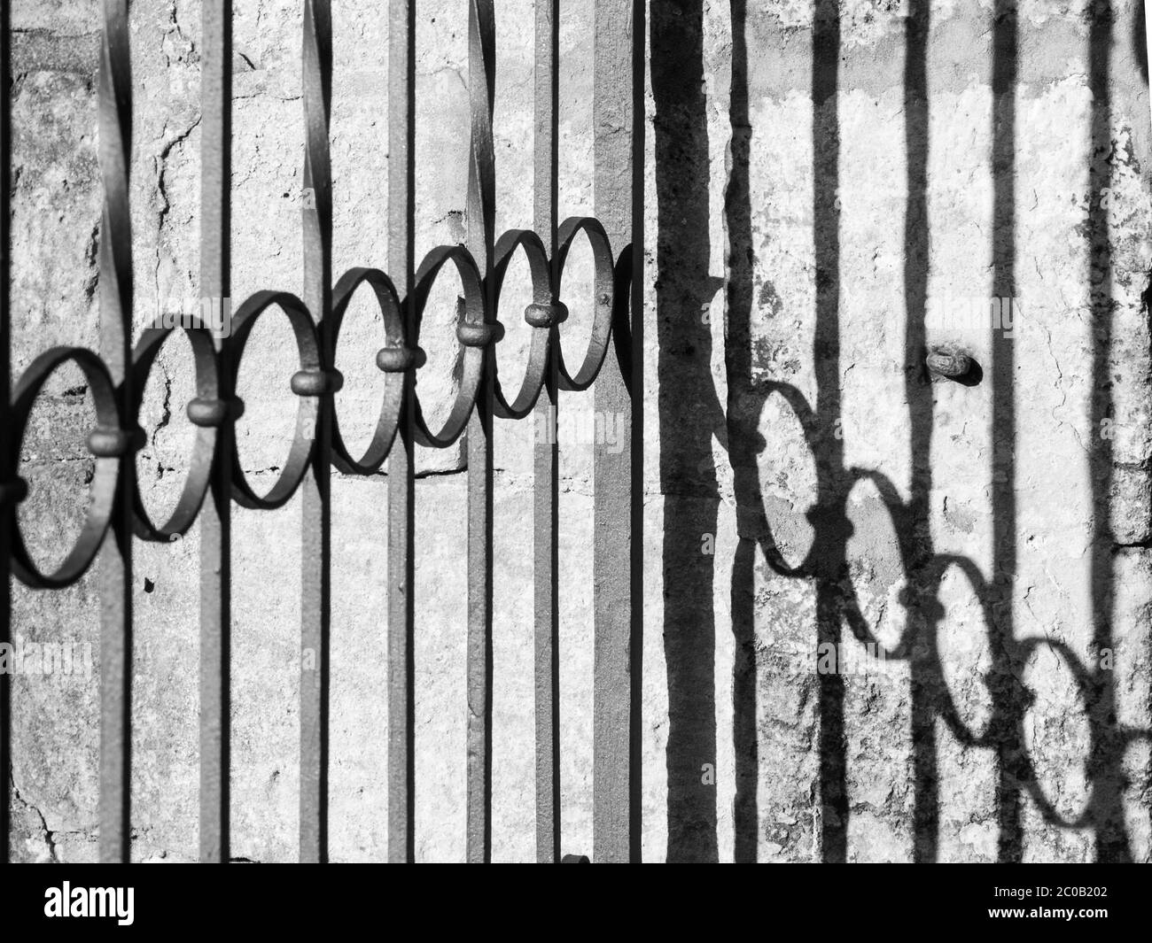 Vista dettagliata del cancello ornamentale in ferro battuto e della sua ombra sul muro. Immagine in bianco e nero. Foto Stock