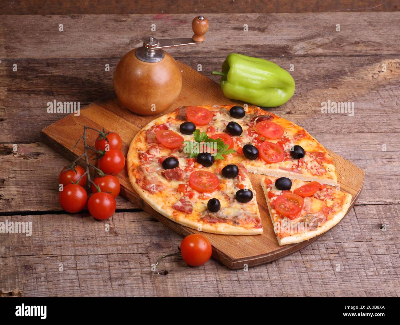 Pezzo di pizza e pizza da un salame, un prosciutto e pomodori su un tavolo di legno Foto Stock