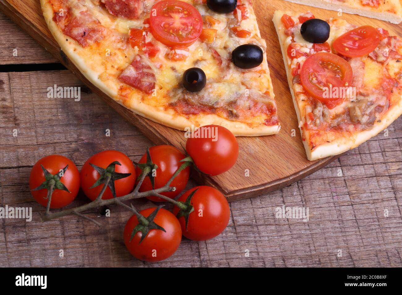 Pezzo di pizza e pizza da un salame, un prosciutto e pomodori su un tavolo di legno Foto Stock