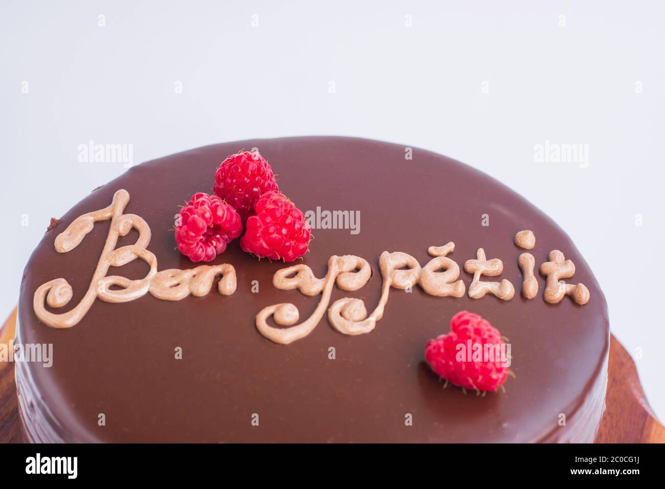 Torta al cioccolato rotonda con decorazioni in lampone e l'iscrizione - Bon appetit. Su un supporto in legno isolato su sfondo bianco. Messa a fuoco selettiva. Foto Stock