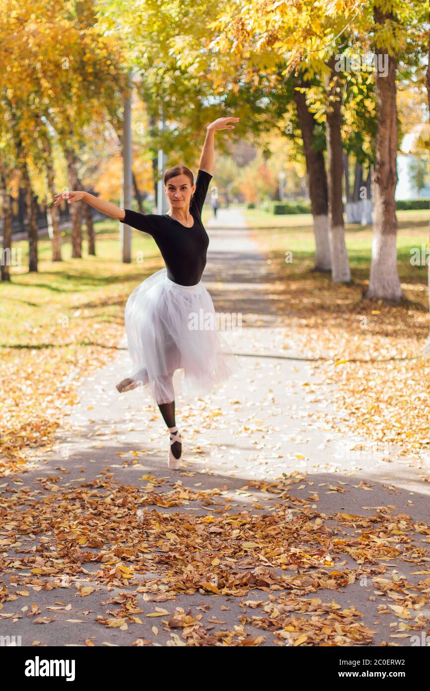 Ballerina donna in una gonna bianca balletto che balla con scarpe appuntite  in un parco d'autunno dorato su foglie gialle secche Foto stock - Alamy