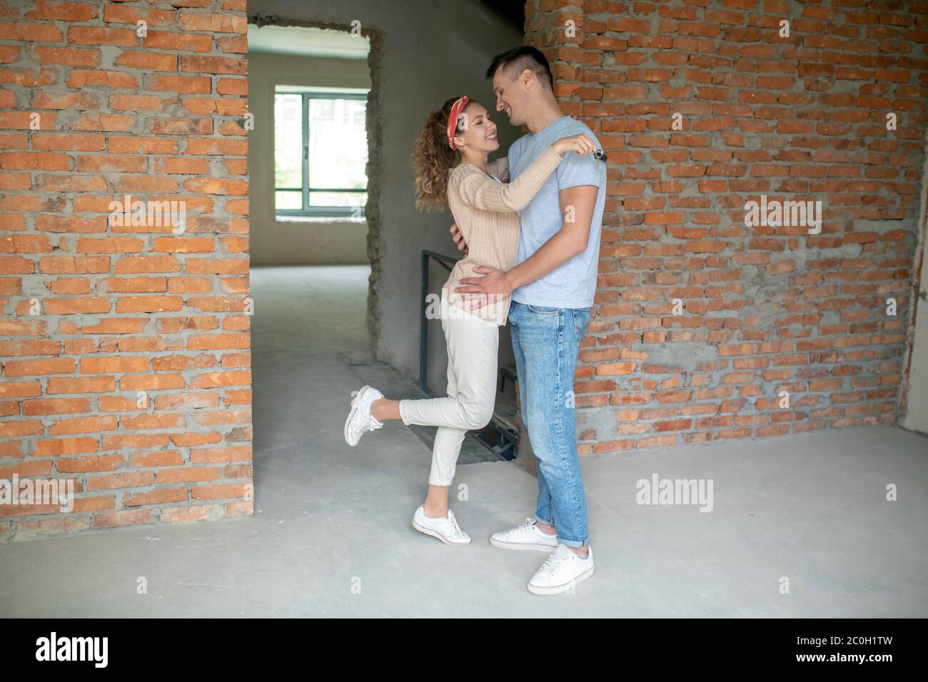 Giovane coppia in piedi nella stanza vuota con pareti di mattoni e abbracciare Foto Stock