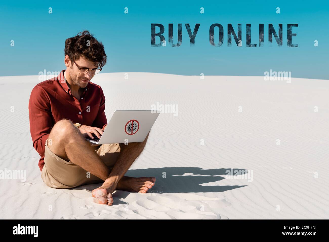 giovane uomo sulla spiaggia di sabbia usando un computer portatile contro il cielo blu chiaro, acquistare illustrazione online Foto Stock