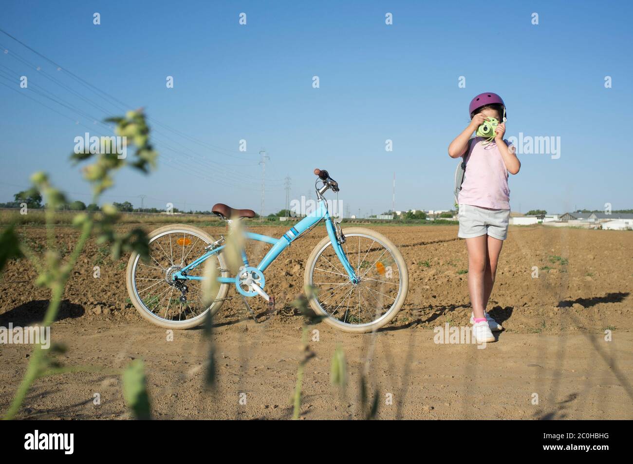 Carina bambina che scatta in campagna con la sua fotocamera istantanea. Ha una bella moto retrò parcheggiata a lato Foto Stock