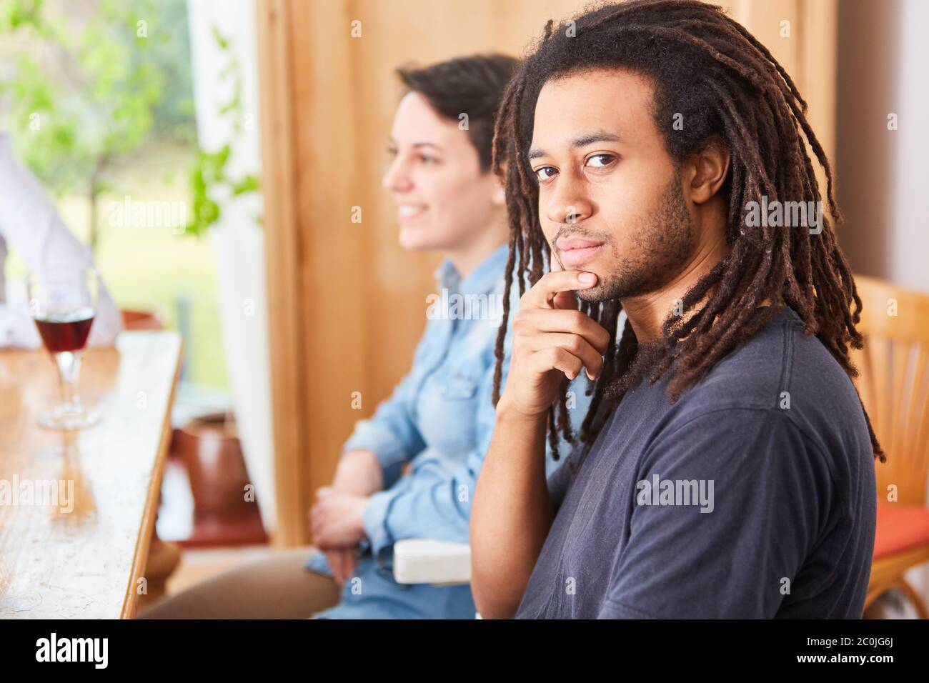 L'uomo africano con i dreadlock siede con gli amici al tavolo a casa Foto Stock