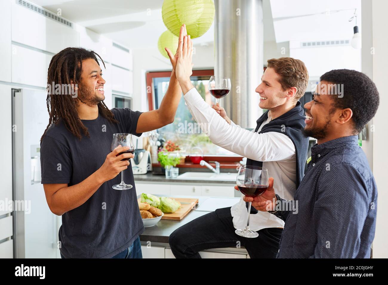Gli amici studenti ridenti si danno cinque in alto a una festa a casa in cucina Foto Stock