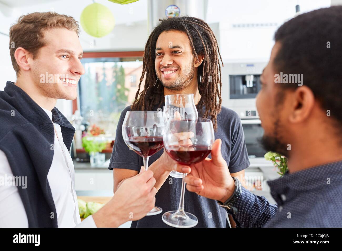 Tre amici che tostano insieme con un bicchiere di vino rosso in cucina Foto Stock