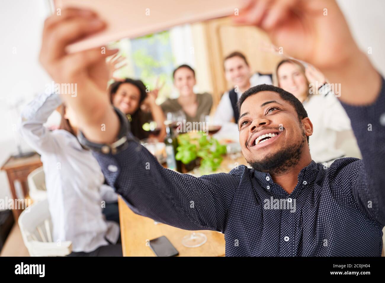 L'uomo effettua selfie o videochiamata con lo smartphone mentre mangia con gli amici al tavolo Foto Stock