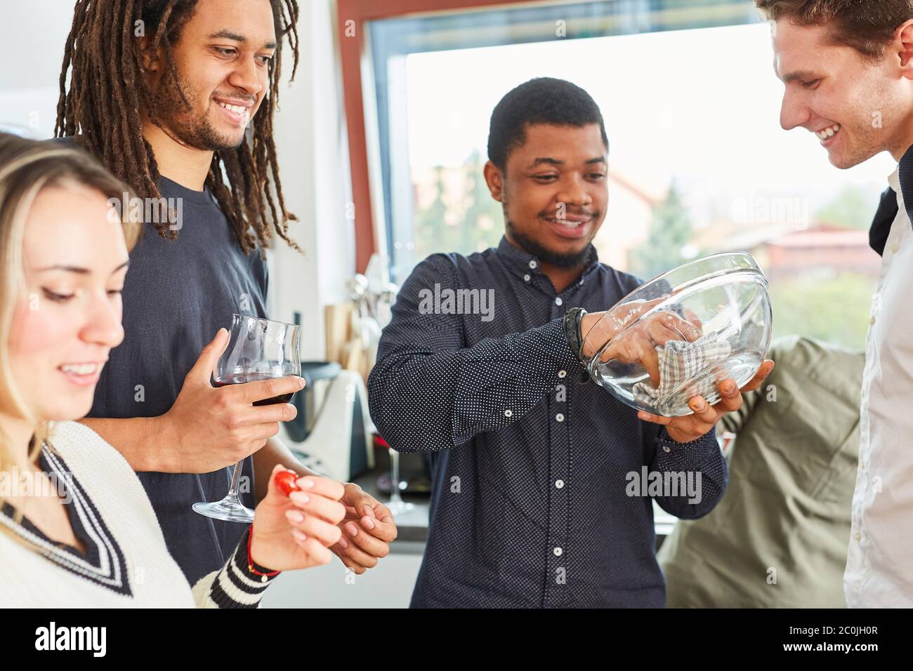 Uomo con asciugamano da tè con gli amici in cucina in appartamento condiviso Foto Stock