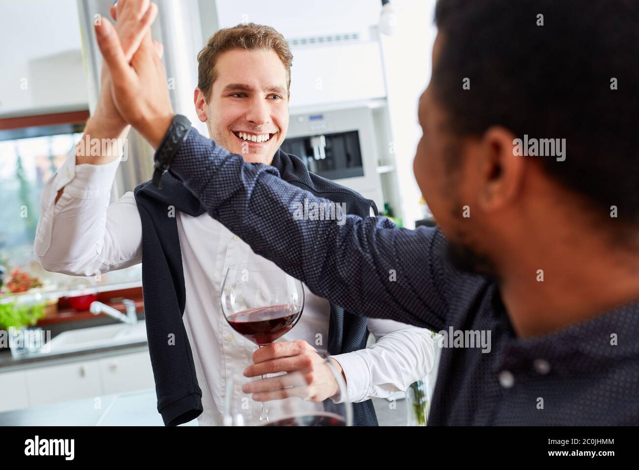 Gli uomini come amici si danno un cinque alto con un bicchiere di vino a casa in cucina Foto Stock