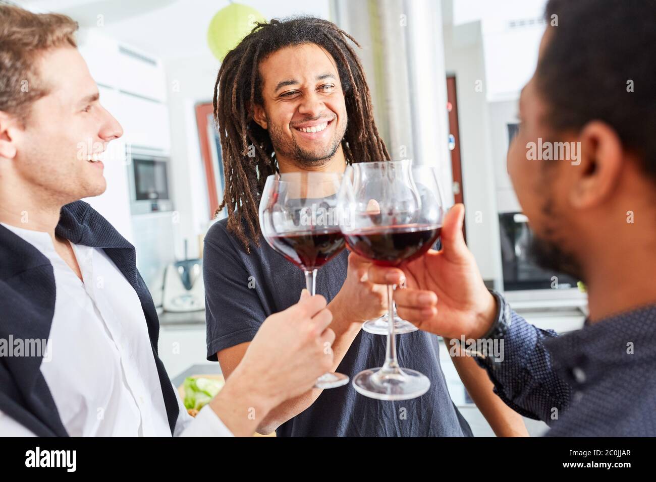 Africano con dreadlock toast con due uomini con un bicchiere di vino rosso a festa Foto Stock