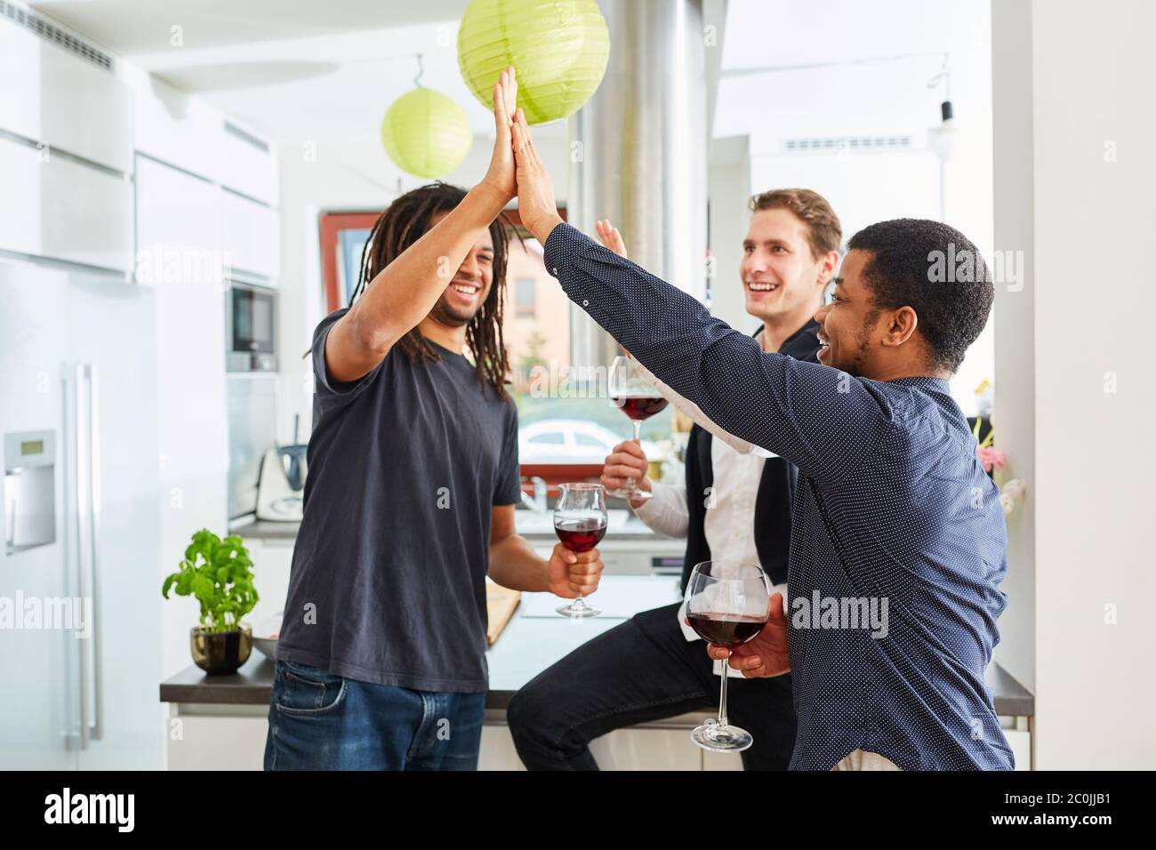 Gruppo di amici che salutano con cinque persone in cucina con un bicchiere di vino rosso Foto Stock