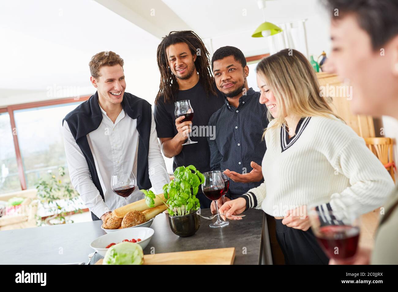 Gli amici ridenti parlano e bevono insieme in cucina durante una riunione Foto Stock