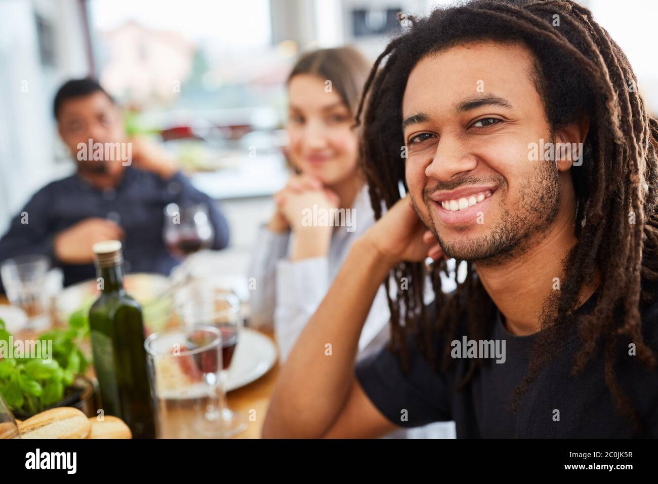 L'uomo africano con i dreadlock siede con gli amici al tavolo da pranzo per un pasto Foto Stock
