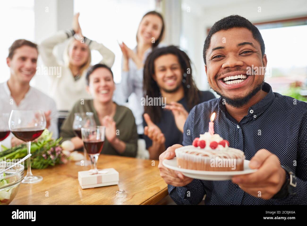Uomo africano che tiene la torta con la candela il suo compleanno alla sua festa di compleanno Foto Stock