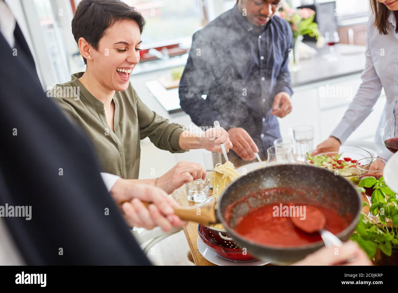 Un gruppo di amici felici serve la pasta con salsa di pomodoro e basilico fresco come pasto Foto Stock