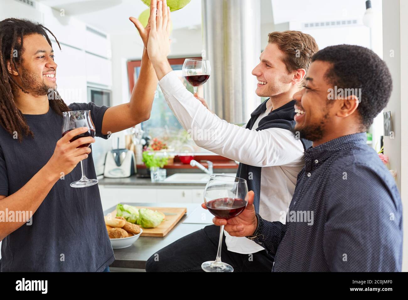 Gli amici studenti ridenti si danno cinque in alto in una festa condivisa a casa in cucina Foto Stock