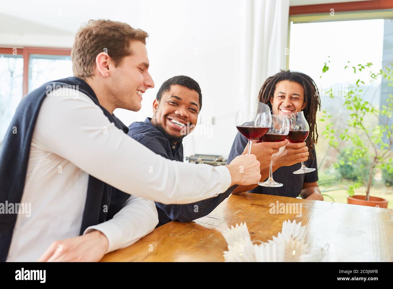 Gruppo di uomini come amici aggrinzire bicchieri di vino rosso e ridere insieme Foto Stock