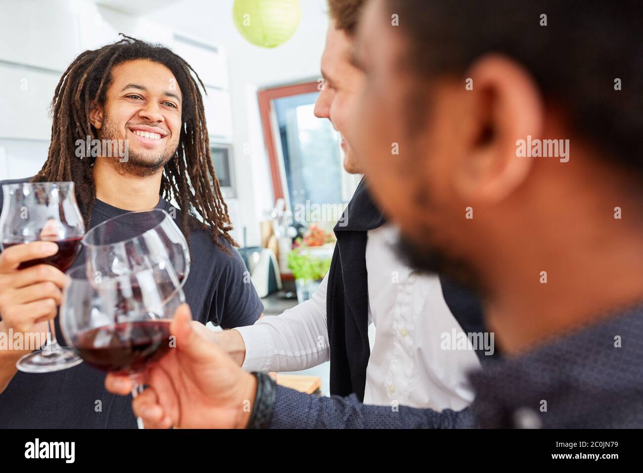 Tre amici che tostano insieme con un bicchiere di vino rosso in una festa in una cucina in comune Foto Stock