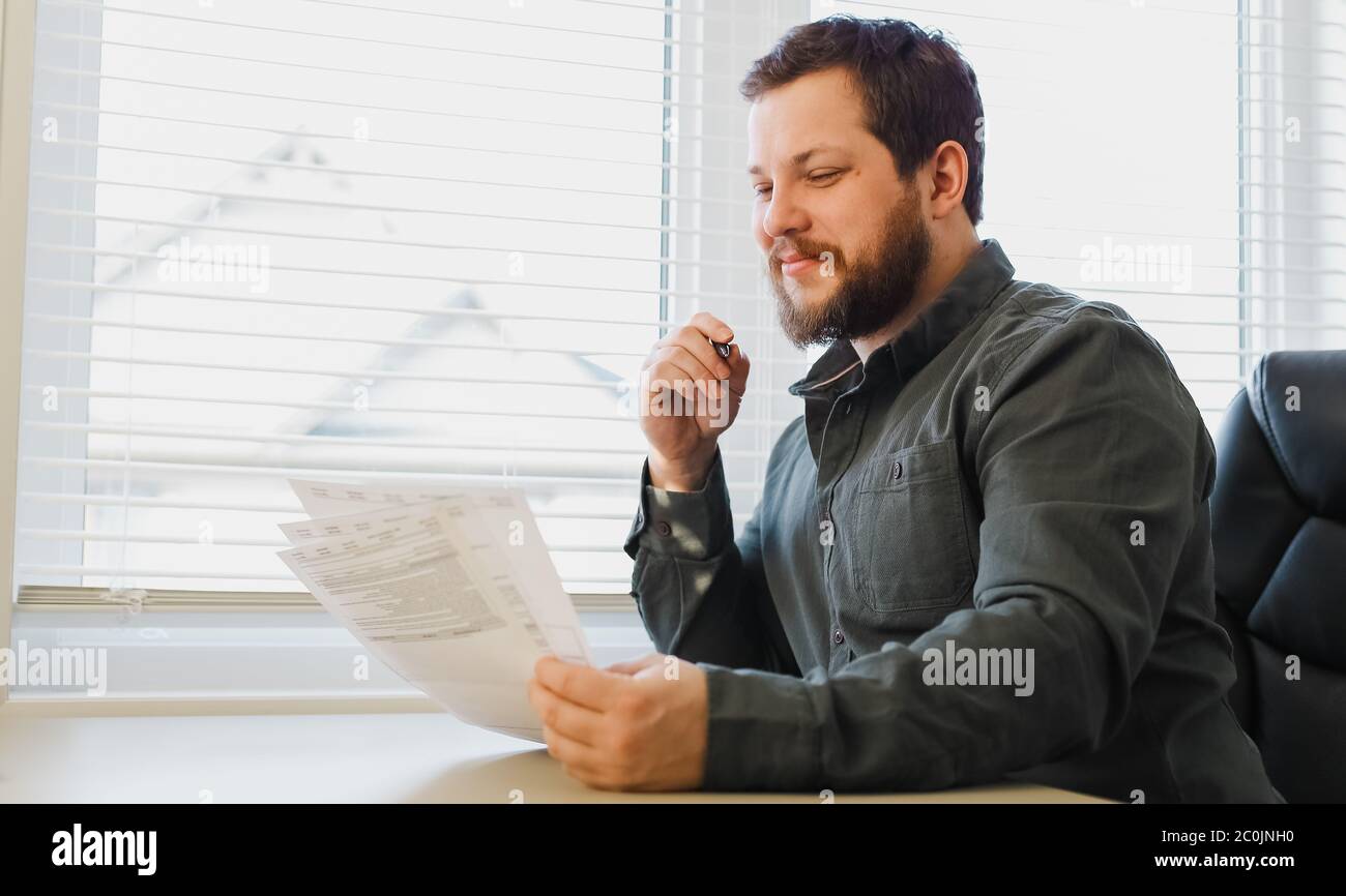Dipendente che compila documenti presso il cabinet, tenendo carte e penne. Foto Stock