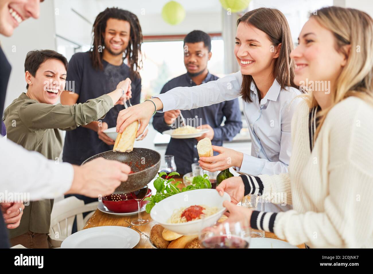 Gruppo di vegani che mangiano nella cucina in comune, spaghetti e contorno Foto Stock