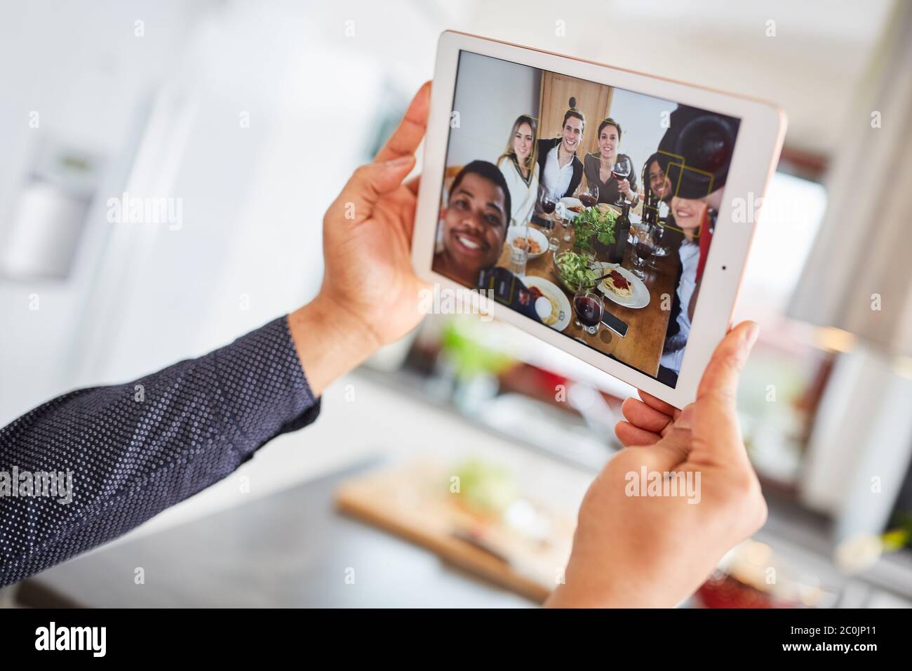 Il gruppo di amici effettua videochiamate in streaming dal vivo utilizzando un tablet mentre si mangia insieme al tavolo Foto Stock
