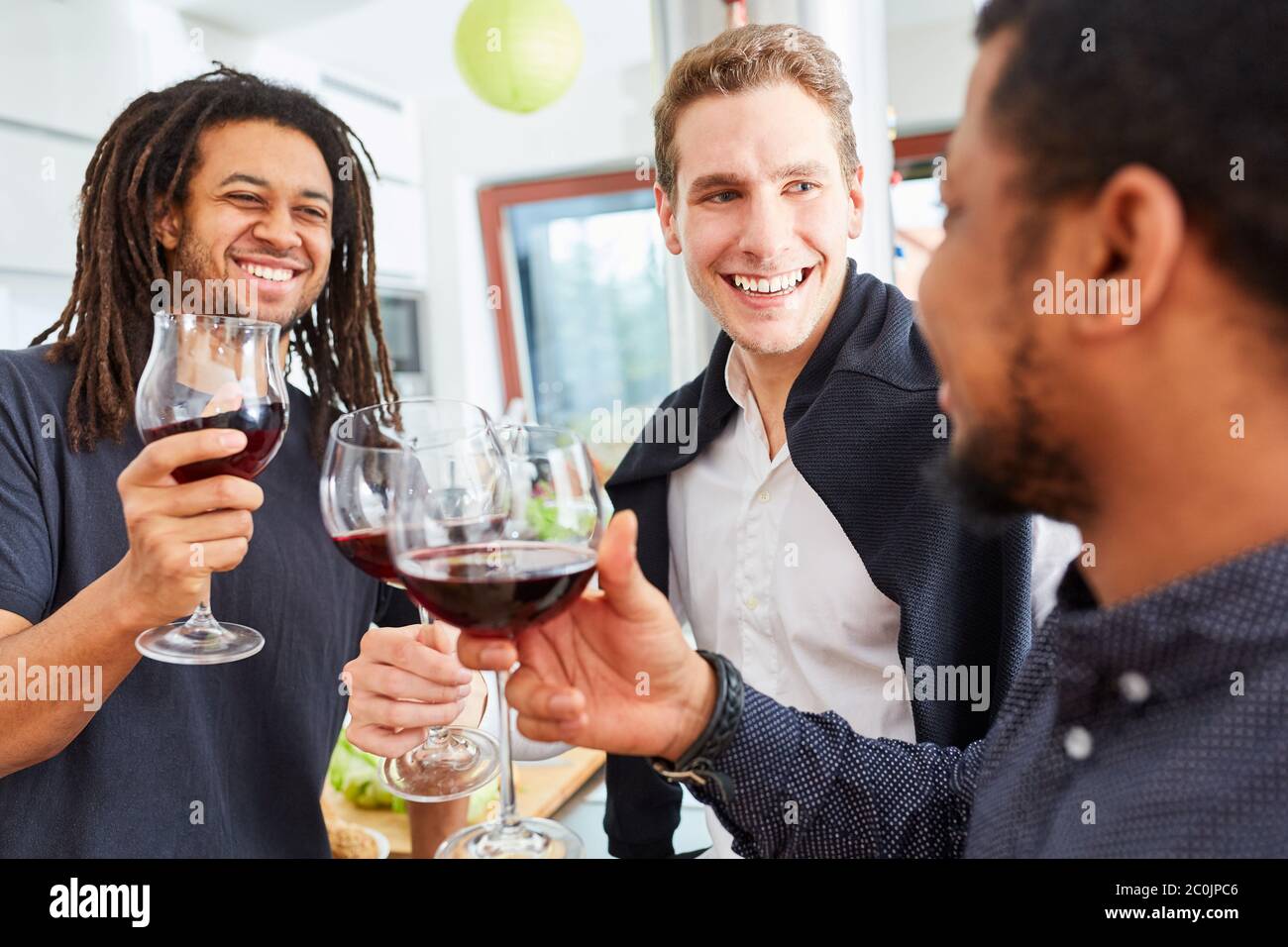 Uomini felici come amici si levano in piedi e bevono il vino insieme nella cucina Foto Stock