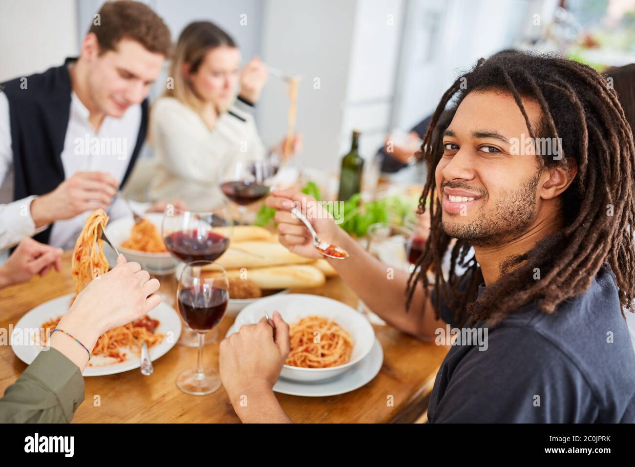 Uomo con temadlock con amici che mangia la pasta insieme nella cucina di un appartamento in comune Foto Stock
