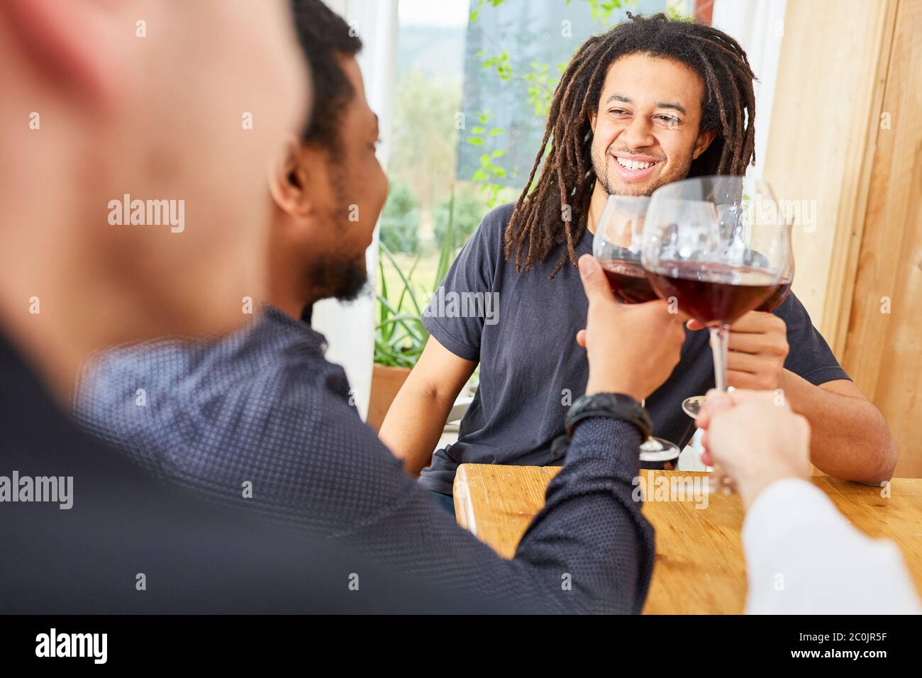 Gli uomini felici come amici brindano insieme con un bicchiere di vino rosso a casa Foto Stock