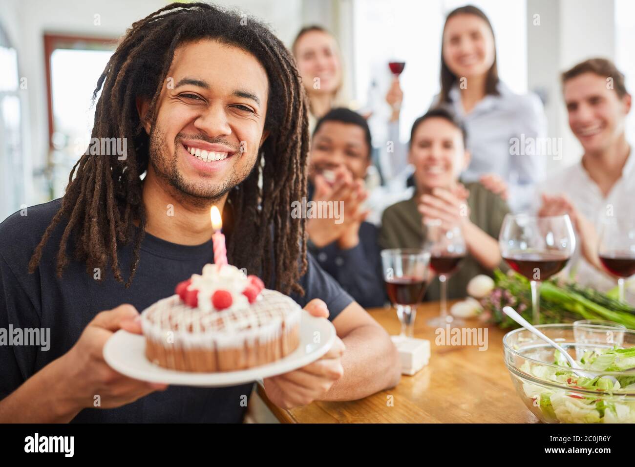 L'uomo con i Dreadlocks tiene la torta con la candela sul suo compleanno alla sua festa di compleanno Foto Stock