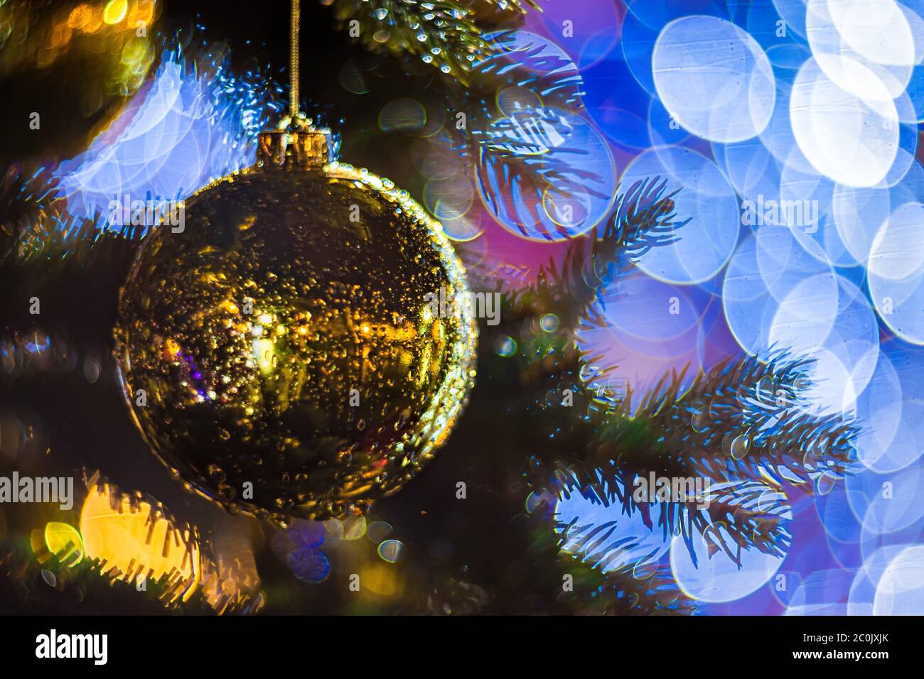 Primo piano di un albero di Natale all'aperto decorato con gusto con una palla d'oro brillante su sfondo sfocato e scintillante. Luci offocate per il ghirlanda, Bokeh eff Foto Stock