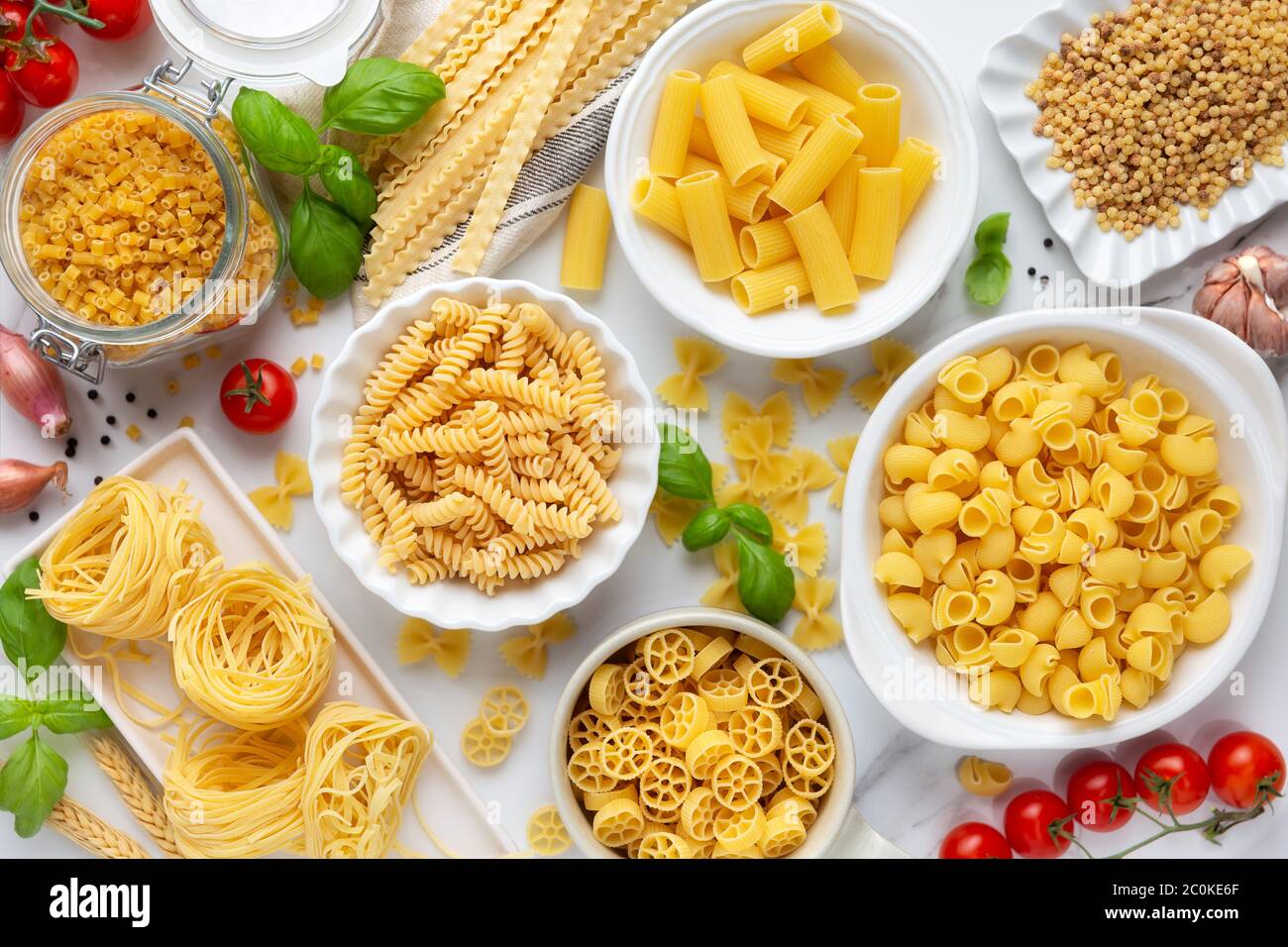 Varietà di tipi e forme di pasta secca - fusilli, penne, nidi di fettuccine, maflaldine, conchiglie, ciotole e ruote - in ciotole bianche con la tradizionale IT Foto Stock