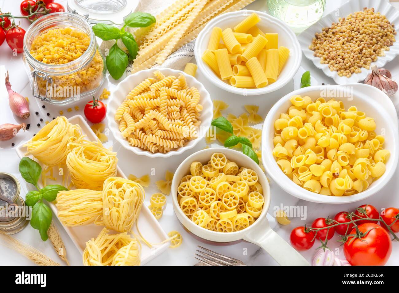Varietà di tipi e forme di pasta secca - fusilli, penne, nidi di fettuccine, maflaldine, conchiglie, ciotole e ruote - in ciotole bianche con la tradizionale IT Foto Stock