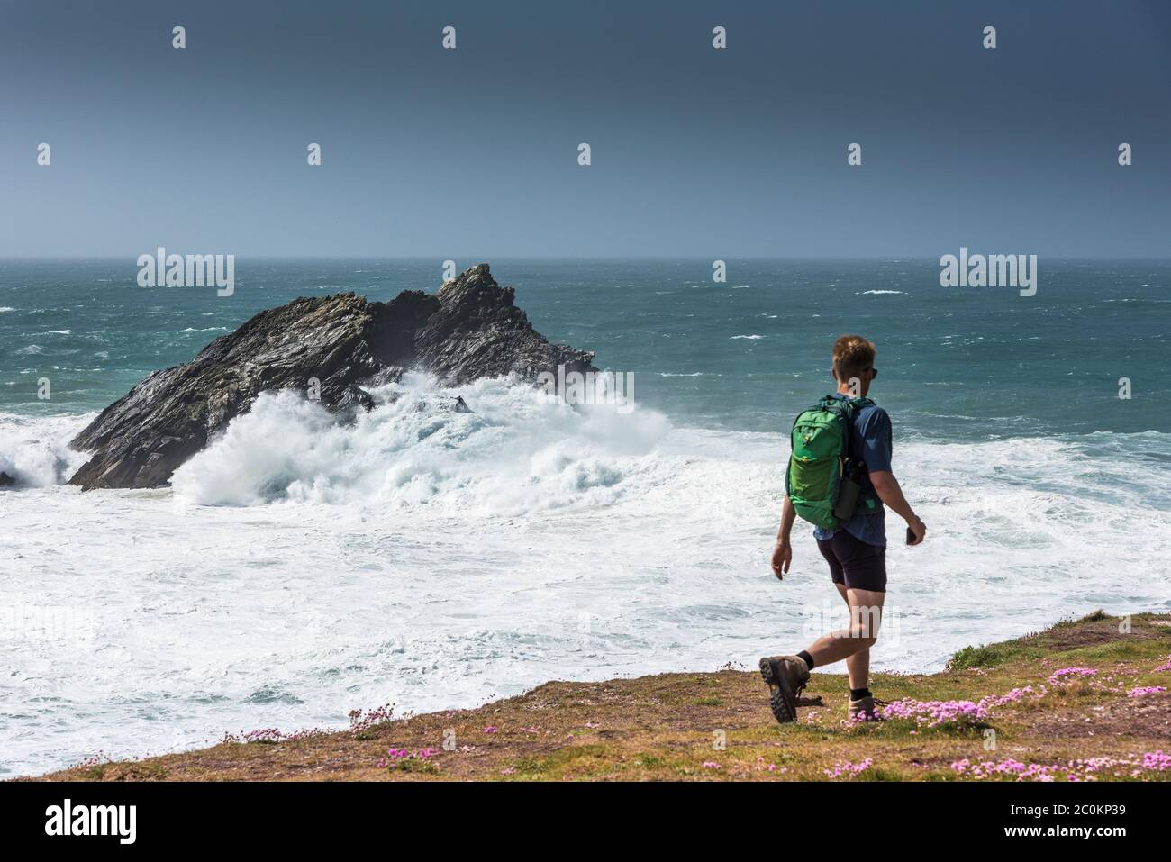 Un camminatore sul percorso della costa come onde selvagge si rompono sopra l'Oca un'isola rocciosa disabitata al largo della costa di Penh Point East a Newquay in Cornovaglia. Foto Stock