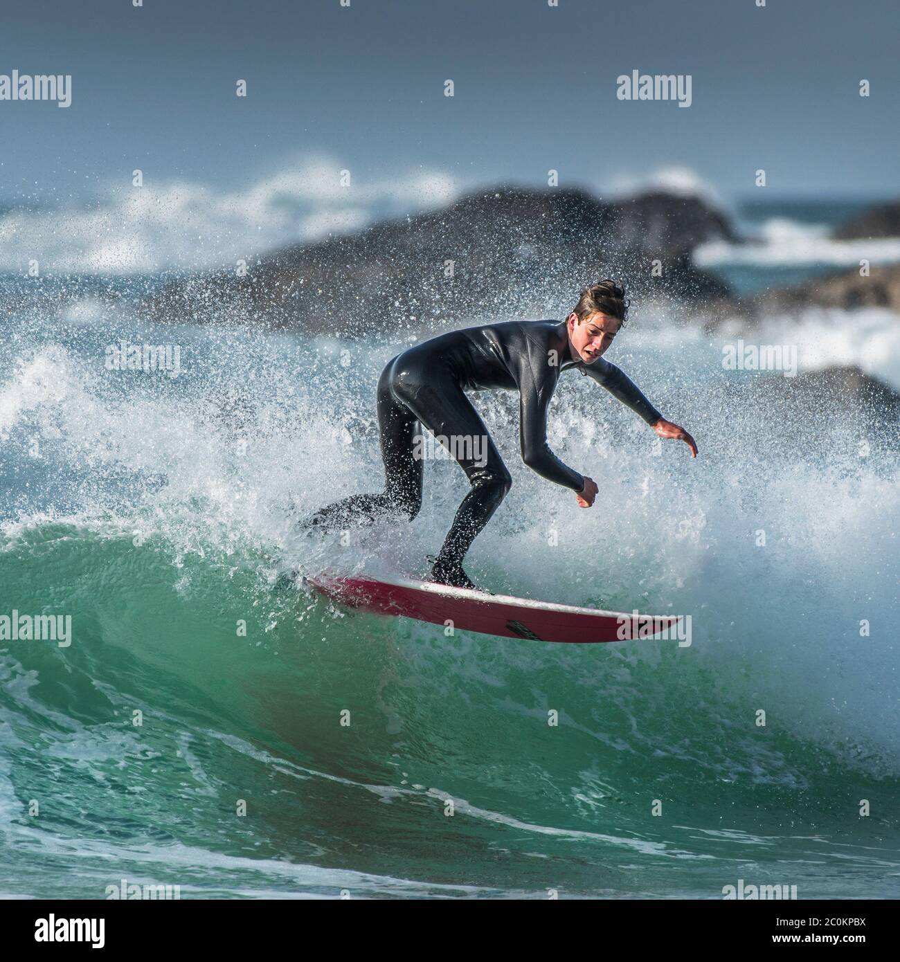 Spettacolare surf azione come un giovane surfista maschio cavalcare un onda a Fistral a Newquay in Cornovaglia. Foto Stock