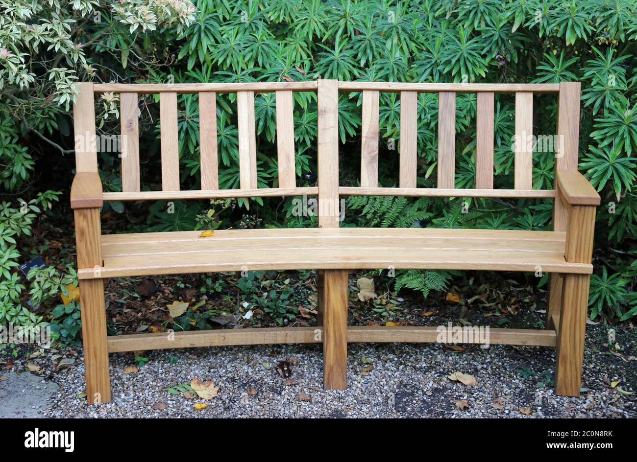 Tradizionale panca curva in legno su una superficie di ghiaia dura con piante arbustive sullo sfondo. Foto Stock