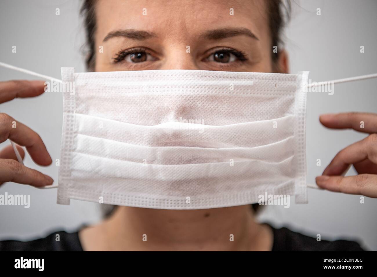 Primo piano ritratto di bella bruna 30s giovane donna coprire il viso indossando maschera medica facciale, anti-virus infezione malattia focolaio protectio Foto Stock