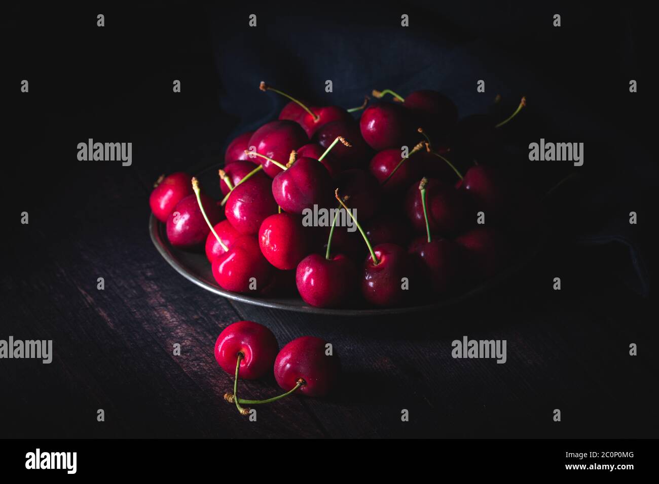 Ciliegie rosse scure su un piatto di peltro. Scarsa illuminazione, composizione orizzontale. Foto Stock
