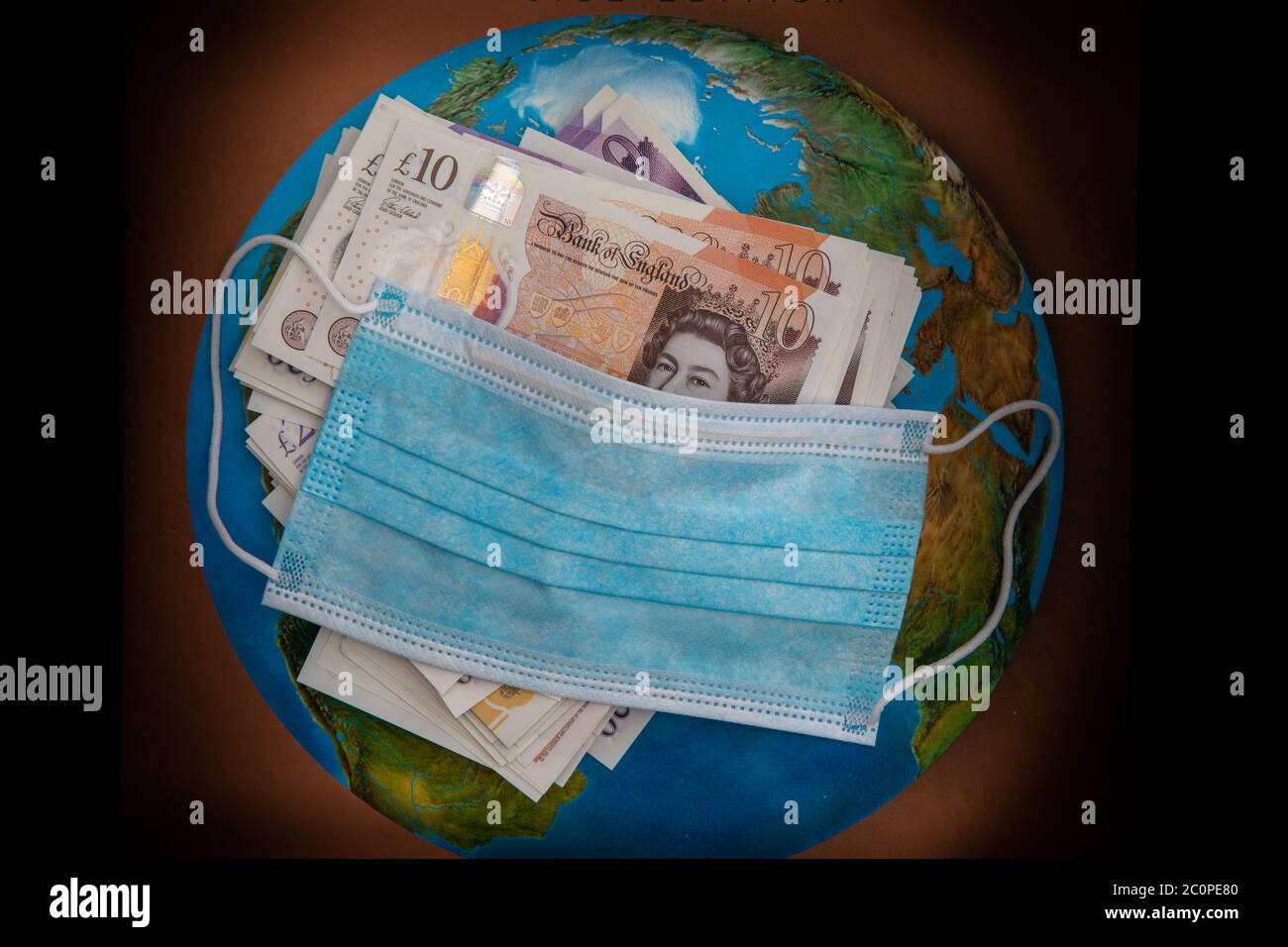 Global Coronavirus pandemico e crash economico. Virus Facemask contiene banconote britanniche con un background mondiale Foto Stock