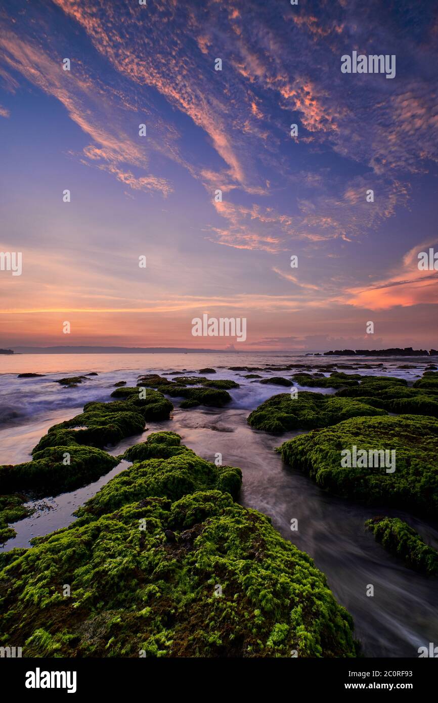 Bella alba su una spiaggia rocciosa coperta da muschio verde con nuvole colorate sul cielo a Sawarna, Banten, Indonesia Foto Stock